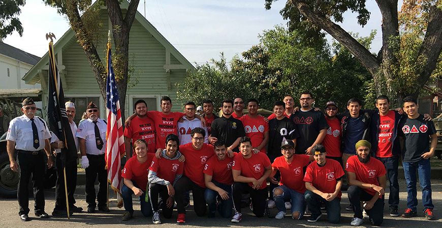 A large group of fraternity members pose in red shirts with uniformed veterans from prior world wars