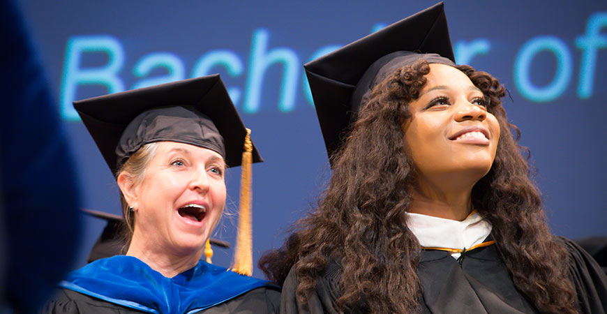 A woman seated, behind the alumna keynote speaker at fall commencement, smiles.